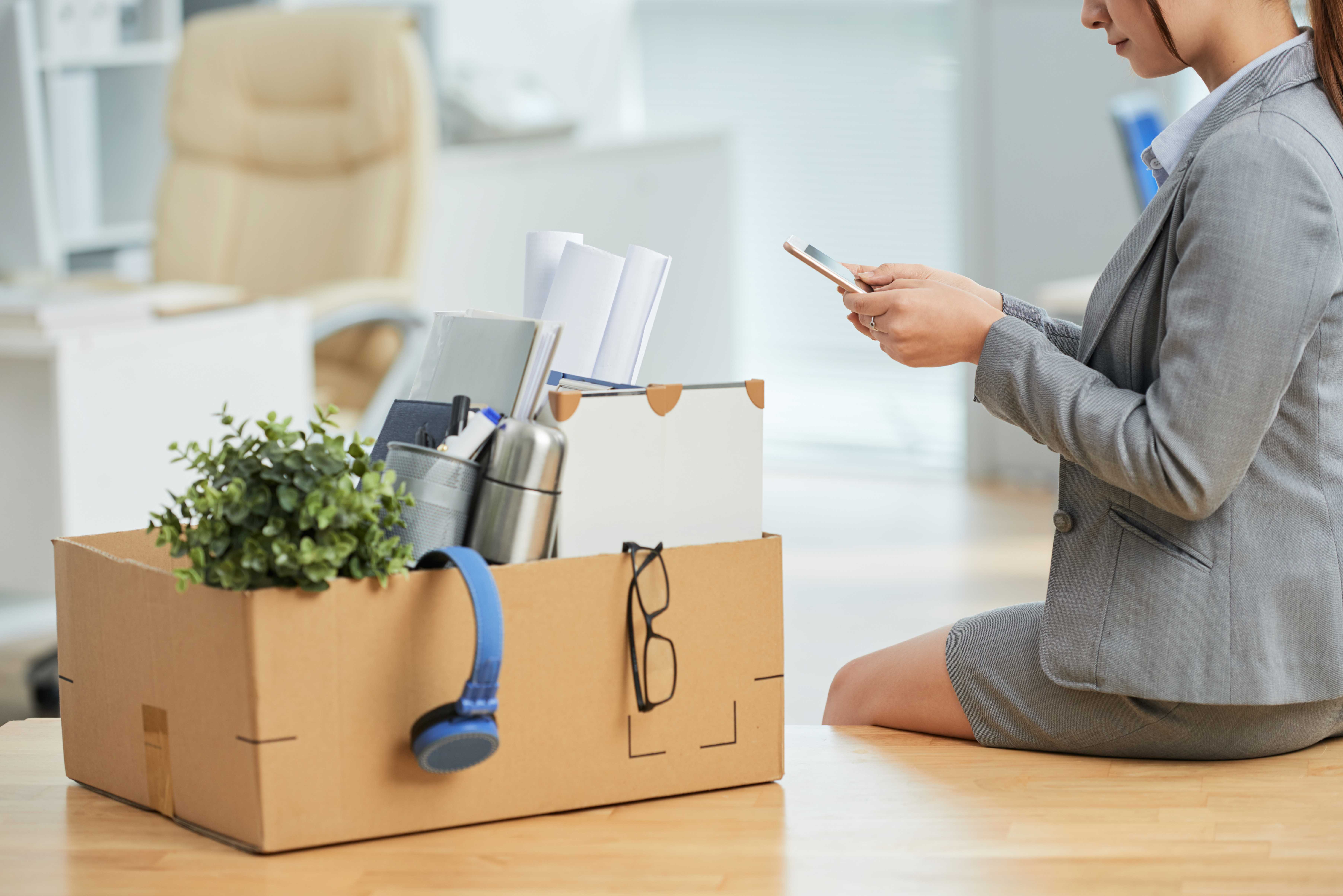 woman-suit-sitting-desk-office-with-belongings-box-using-smartphone.jpg